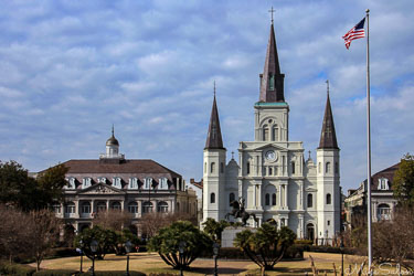 St Louis Cathedral in New Orleans with three spires, flanked by historic buildings and gardens of Jackson Square under a bright blue sky.
