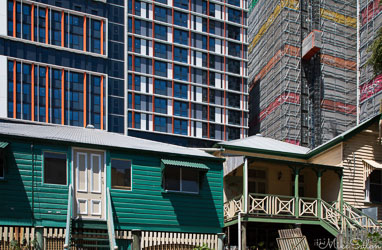 Traditional wooden Queenslander houses in front of modern high‑rise buildings in Brisbane, showing contrast between old and new architecture.