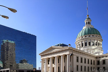 St Louis Old Courthouse with green dome and white columns, framed by a modern glass skyscraper and clear blue sky.